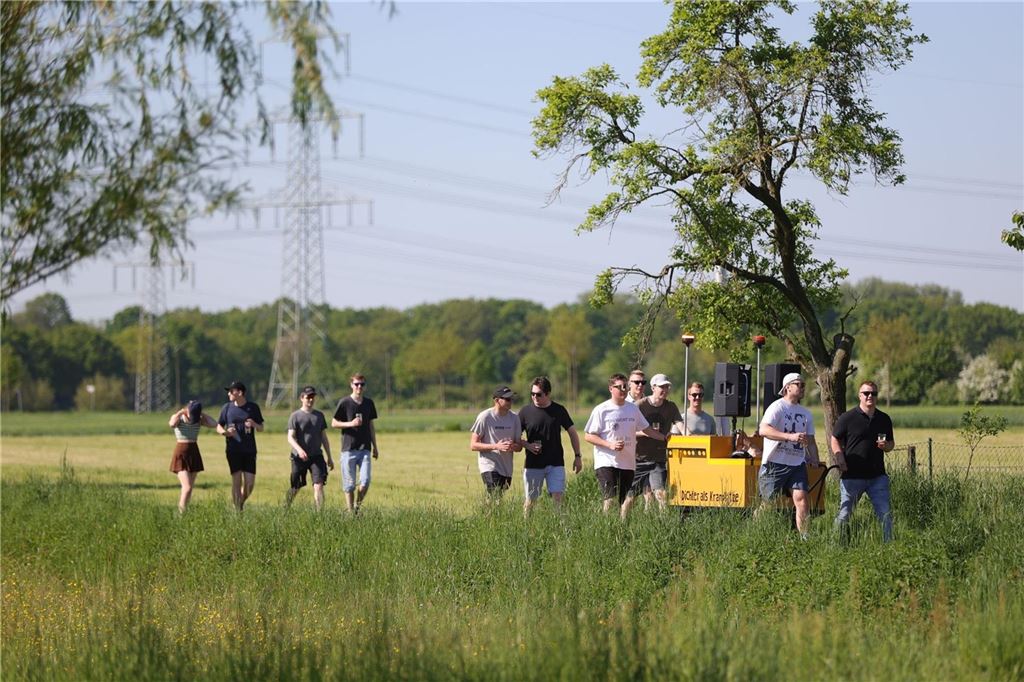 Tausende feiern den 1. Mai: Kreative Wagen, weite Anreisen und beste Laune Menschen wandern an einem Feld vorbei mit einem gelben Bollerwagen.