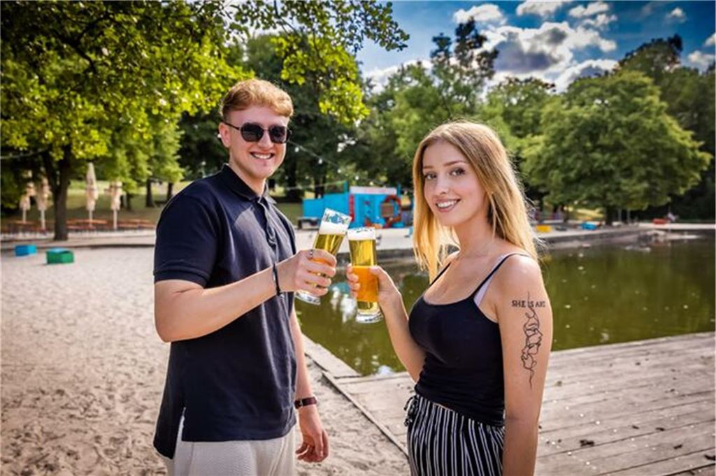 Eröffnungstermin für Strandbar „Pilina Beach“ im Revierpark steht fest Zwei junge Menschen stoßen in der Strandbar im Revierpark Wischlingen mit Bier an.