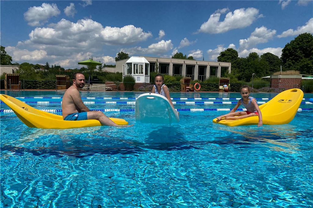 Mit dem Rad, Auto oder dem Bus in die Freibäder der Umgebung Drei Badegäste sitzen auf schwimmenden Liegen.