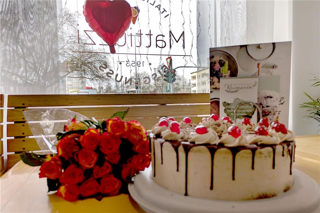Was ist los bei Mattiuzzi? Anzeige schreckte Kunden der Eisdiele auf Eine Schoko-Kirsch-Torte steht neben einem Strauß roter Rosen auf einem Tisch.