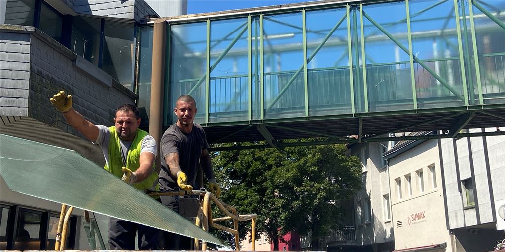Abriss der Schnückel-Brücke gestartet: Sperrung überrascht Passanten Zwei Arbeiter werfen die Scheiben der Schnückel-Brücke in einen Container. Die Abrissarbeiten der Fußgängerbrücke sind am Montag gestartet.