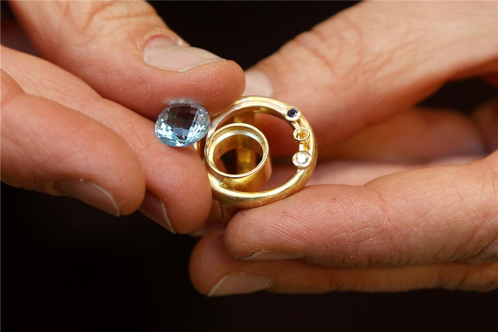 Zwei Eheringe, die zu einem Ring verarbeitet werden. Daneben ist eine Zeichnung, wie die Arbeit der Goldschmiedin Stephanie Telgmann am Ende aussehen soll.