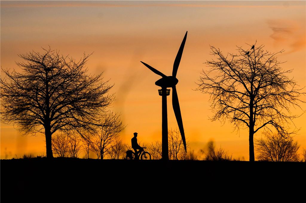 Bau von Windrädern bei Hemmerde genehmigt: Acht Jahre nach dem Antrag Ein Mann fährt bei Sonnenaufgang mit einem Fahrrad über einen Feldweg – im Hintergrund ist ein Windrad zusehen.